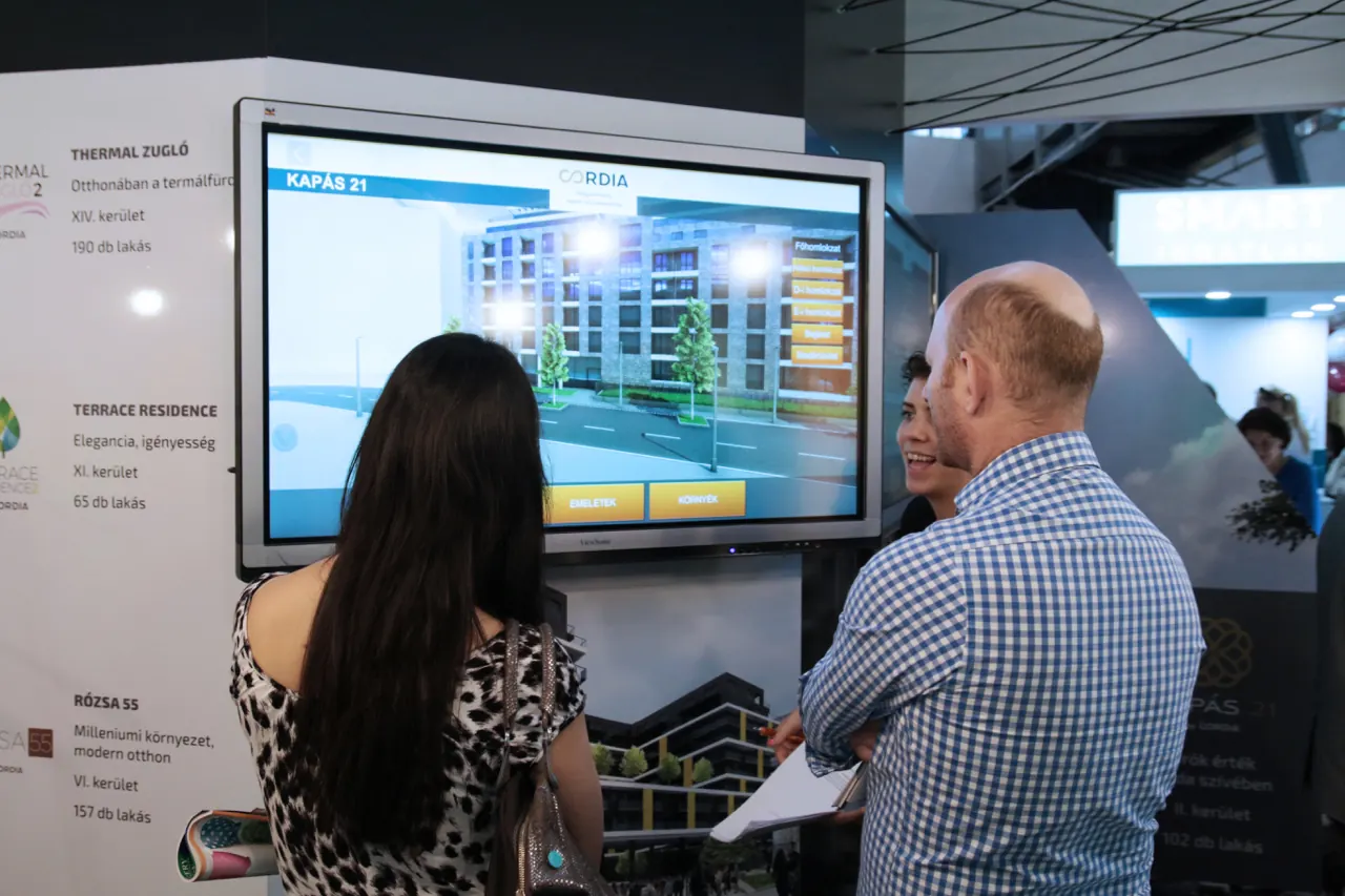 Two visitors look at the model of a planned building on a large touchscreen